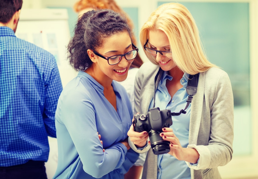 business, photography and startup concept - two smiling young women looking at digital camera at office